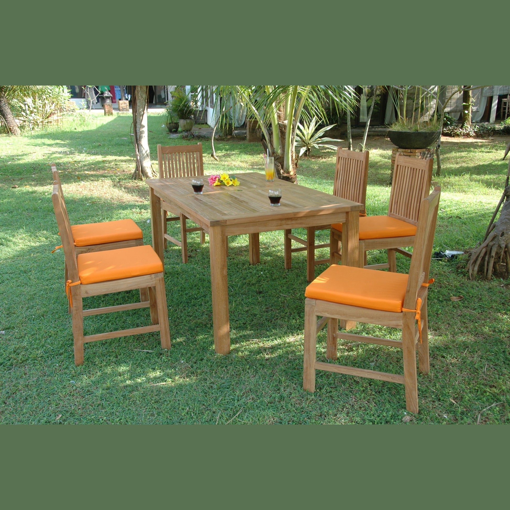 Wooden dining table with four chairs and orange cushions on a grassy area