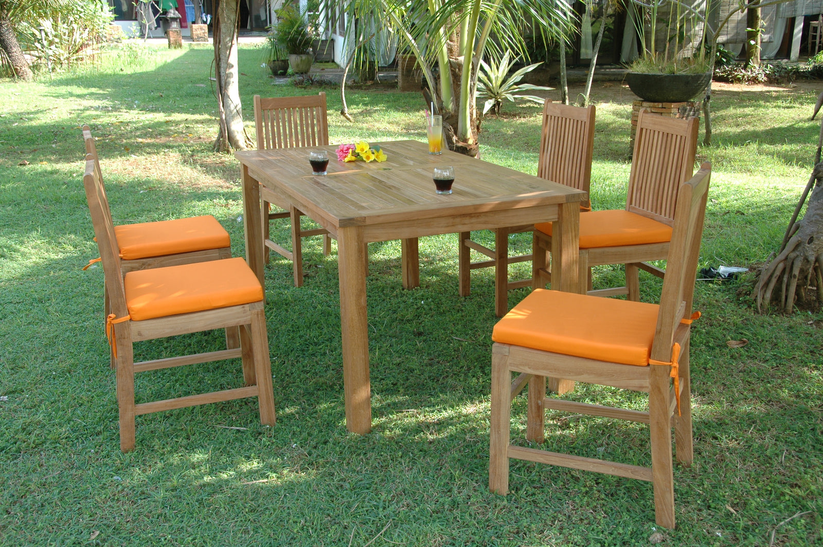 Wooden dining table with four chairs and orange cushions on a grassy area