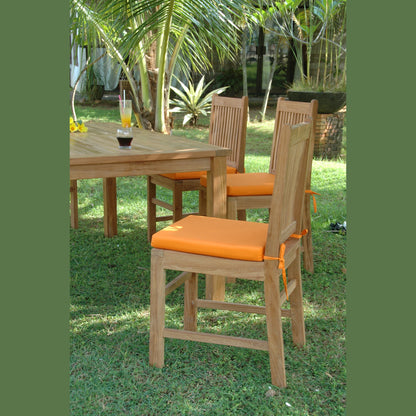 Outdoor setting with wooden table and chairs with orange cushions on a grassy area.