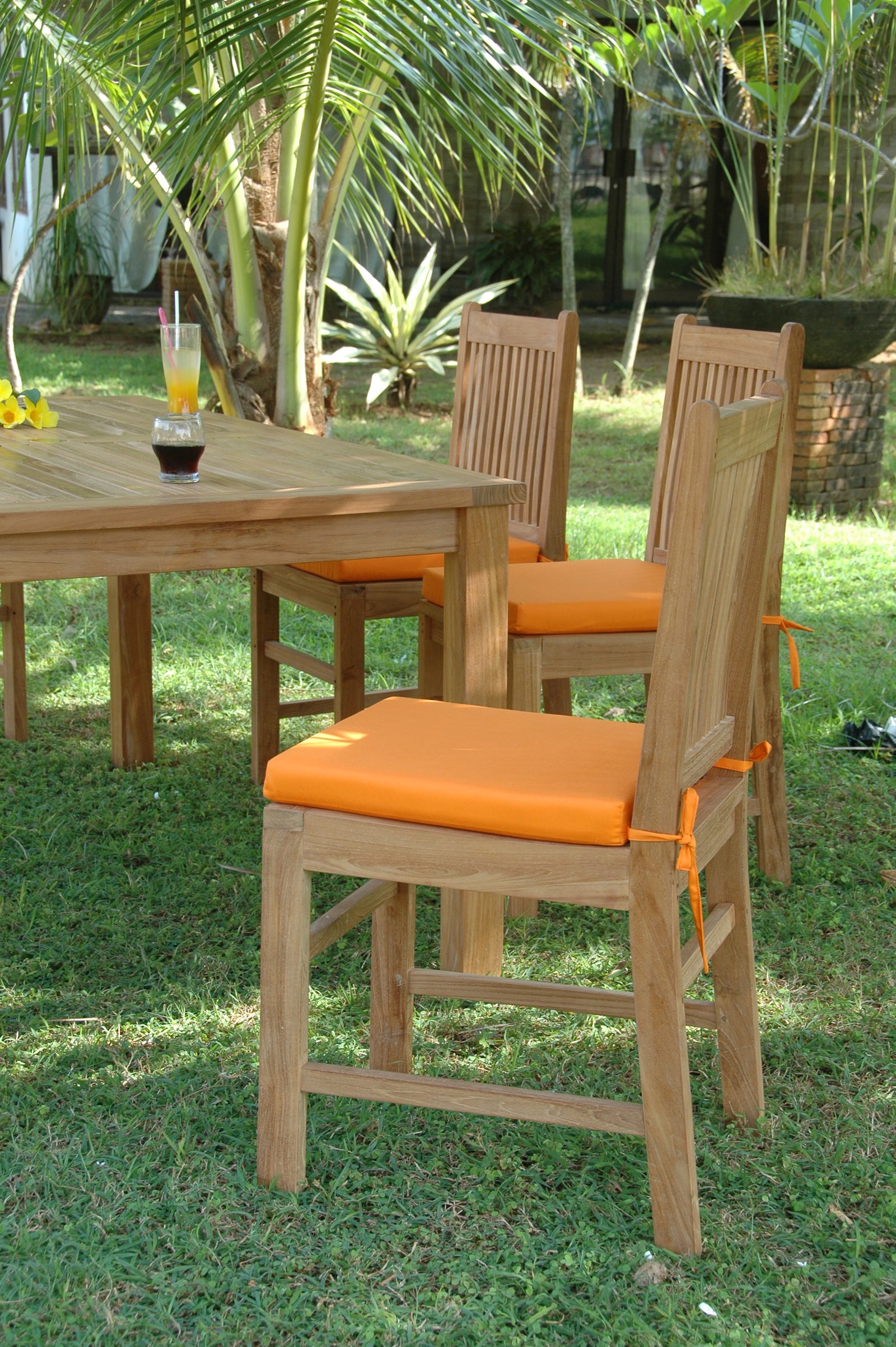 Outdoor setting with wooden table and chairs with orange cushions on a grassy area.