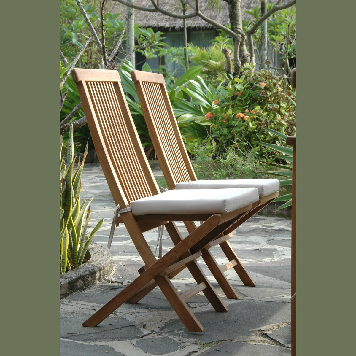 Two wooden folding chairs with white cushions on a stone patio surrounded by greenery.