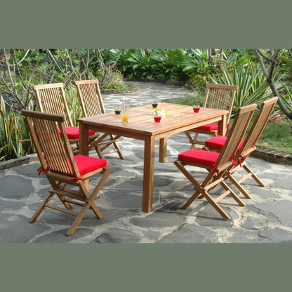 Wooden outdoor dining table with six chairs on a stone patio surrounded by greenery.