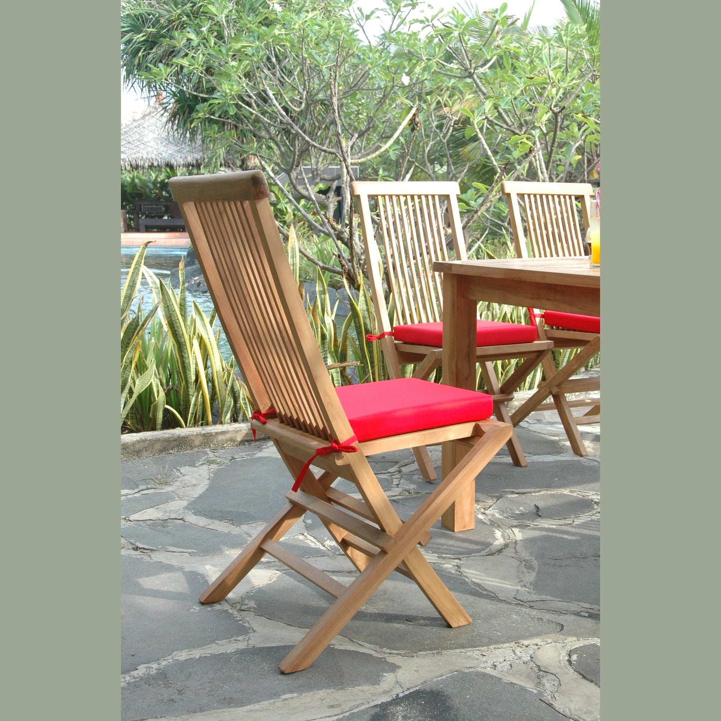 Wooden chairs with red cushions on a stone patio with a garden background