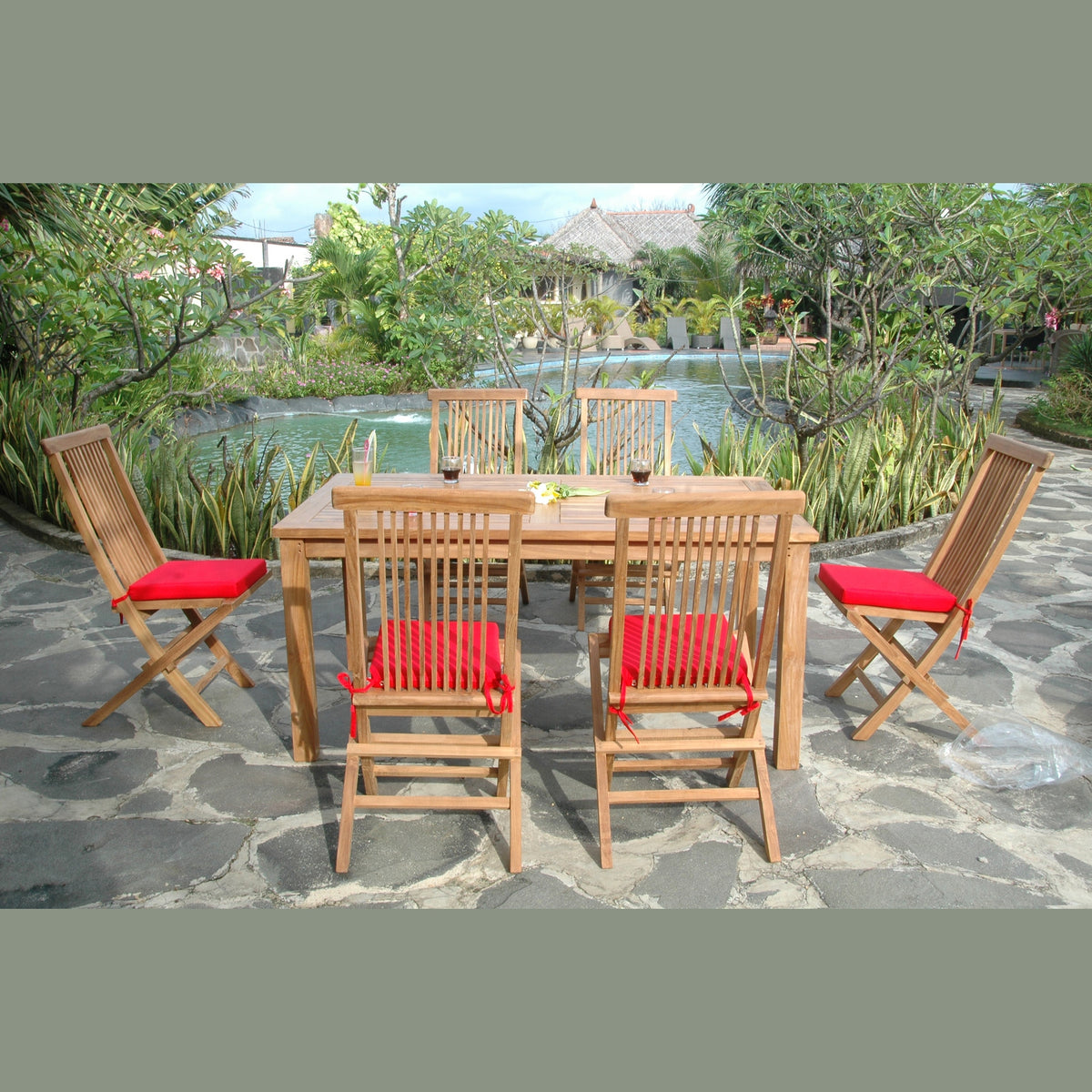 Outdoor wooden dining set with red cushions near a poolside garden.