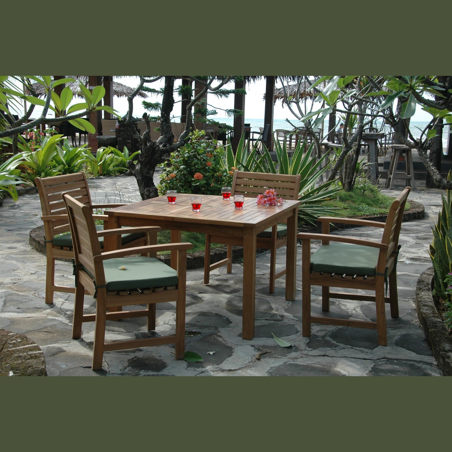 Outdoor patio set with wooden table and chairs on a stone patio surrounded by plants.
