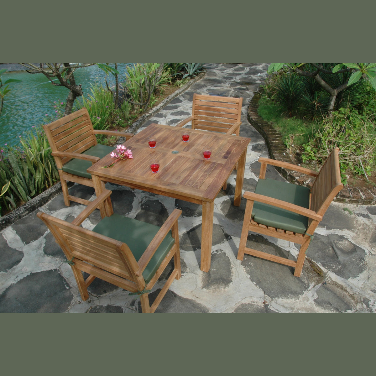 Wooden outdoor furniture set with table and chairs on a stone patio near a body of water.