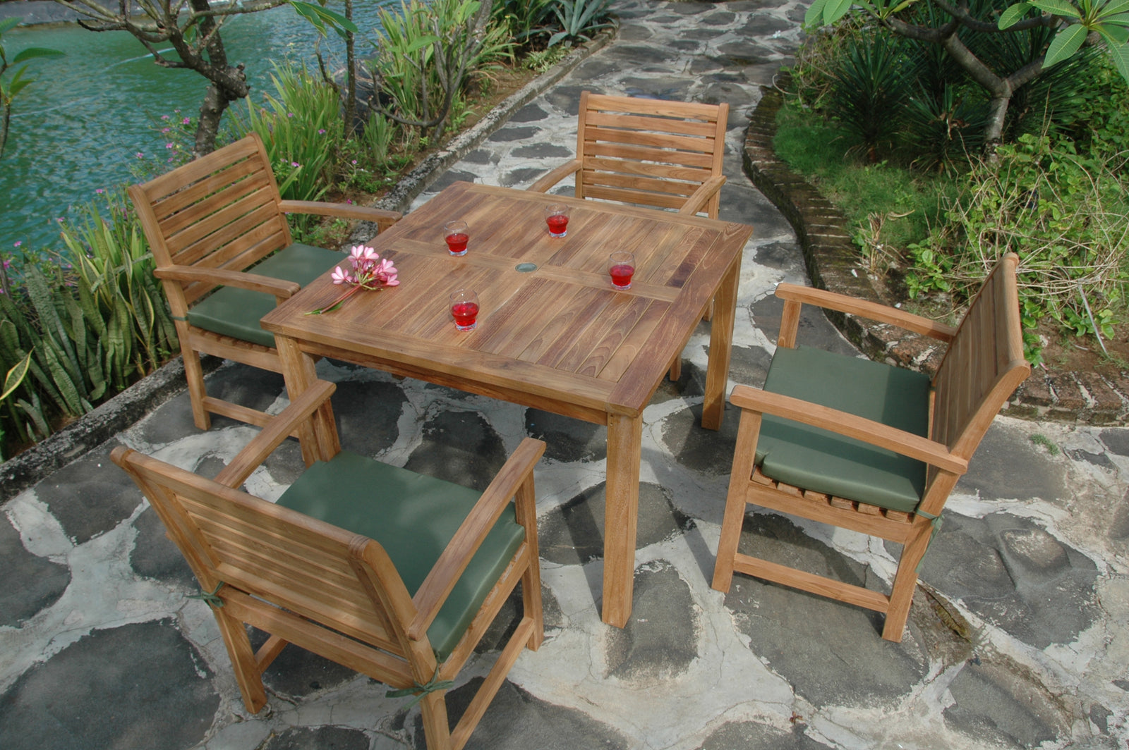 Wooden outdoor furniture set with table and chairs on a stone patio near a body of water.