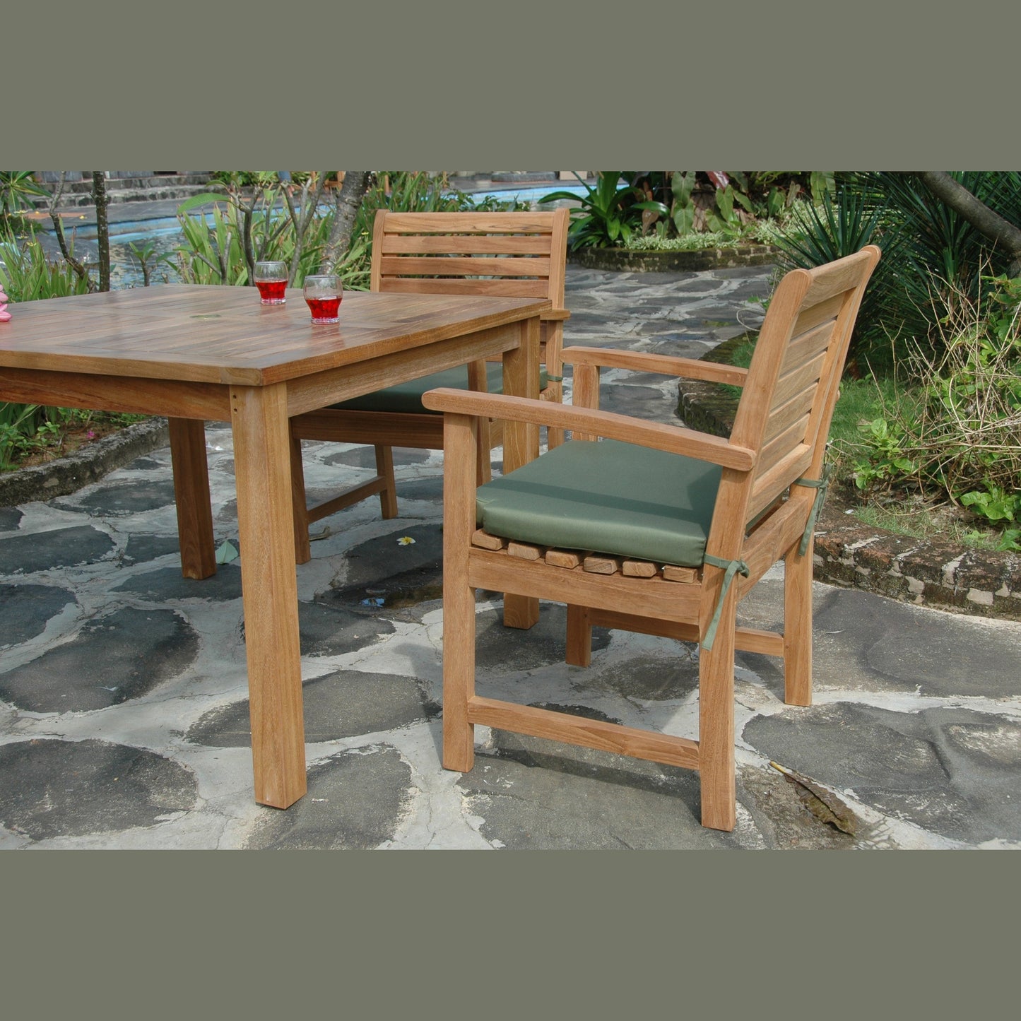 Wooden outdoor dining table and chairs with green cushions on a stone patio.