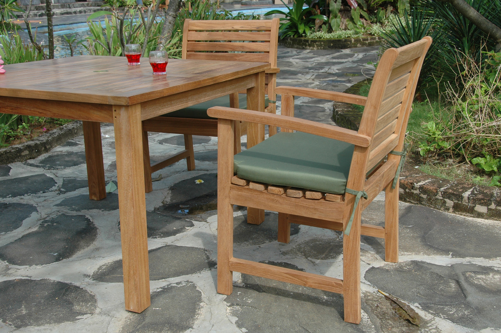 Wooden outdoor dining table and chairs with green cushions on a stone patio.