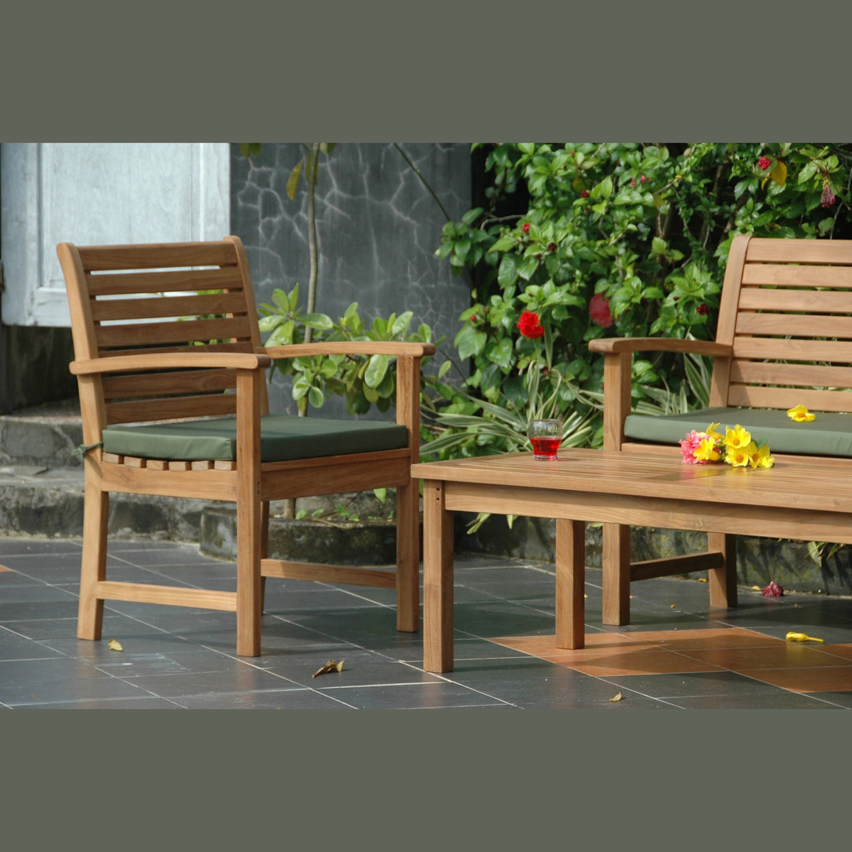 Wooden outdoor chairs with green cushions and a small table with flowers on a patio.