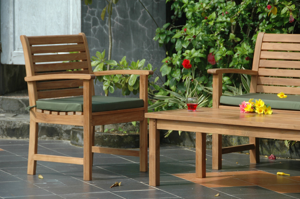 Wooden outdoor chairs with green cushions and a small table with flowers on a patio.