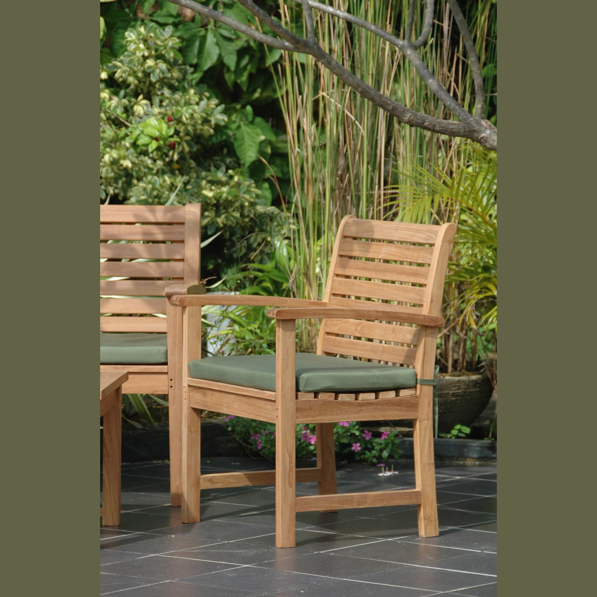 Two wooden chairs with green cushions on a patio with plants in the background