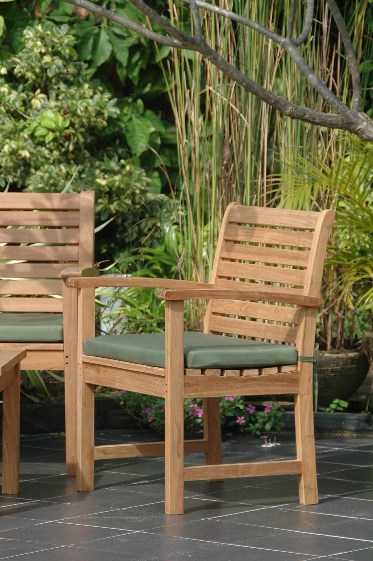 Two wooden chairs with green cushions on a patio with plants in the background
