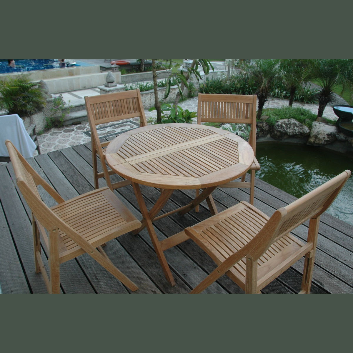 Wooden outdoor dining set with table and chairs on a wooden deck by a pond.