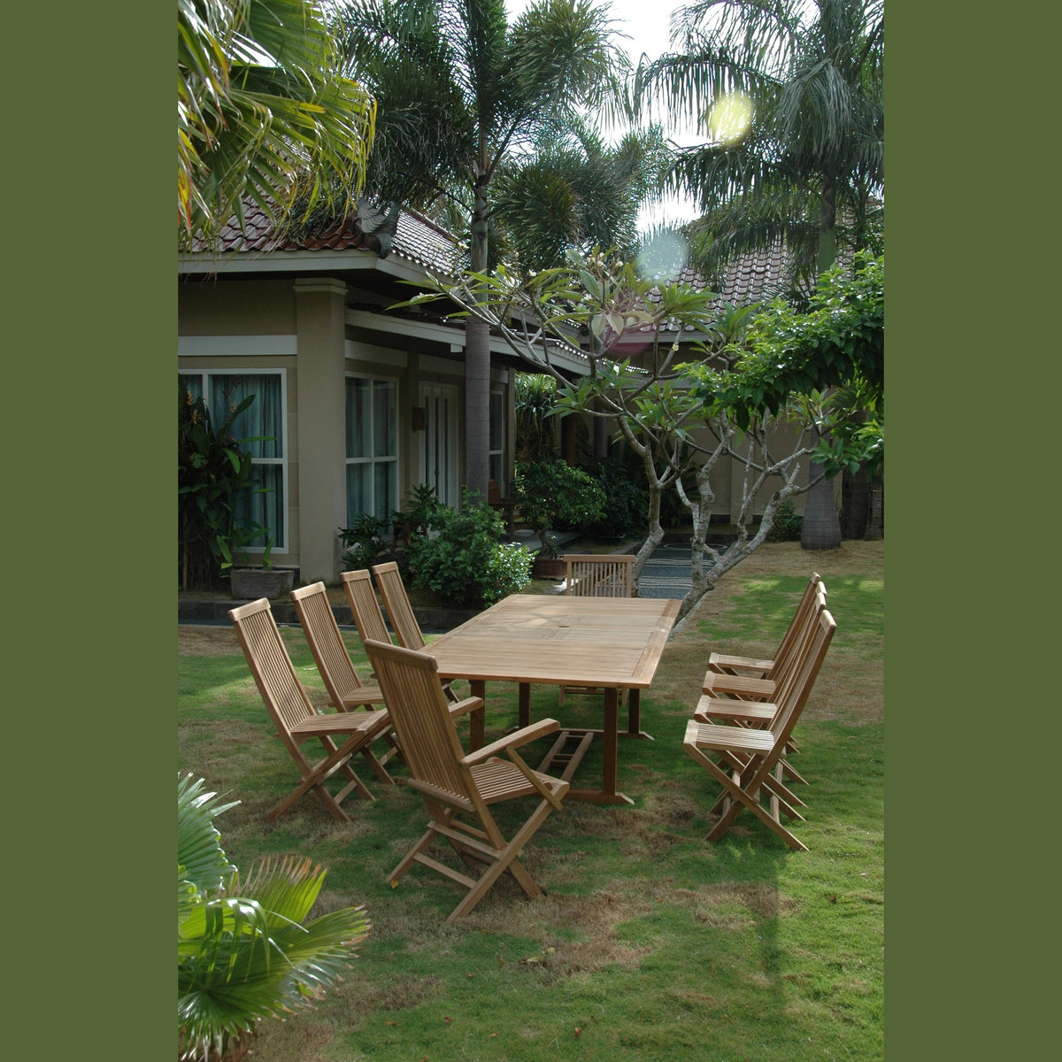 Wooden outdoor dining set with chairs on a grassy area surrounded by trees and a building.