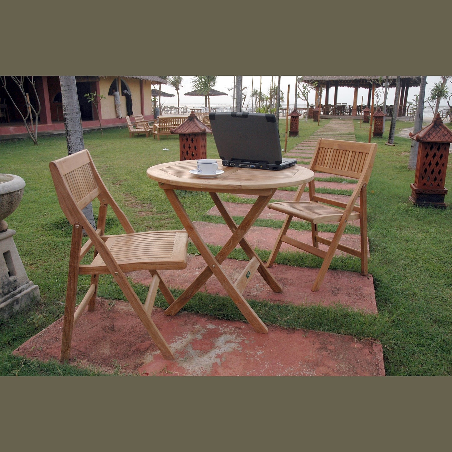 Wooden outdoor table with chairs and a laptop on a grassy area.