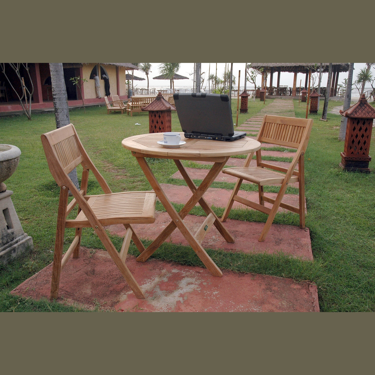 Wooden outdoor table with chairs and a laptop on a grassy area.