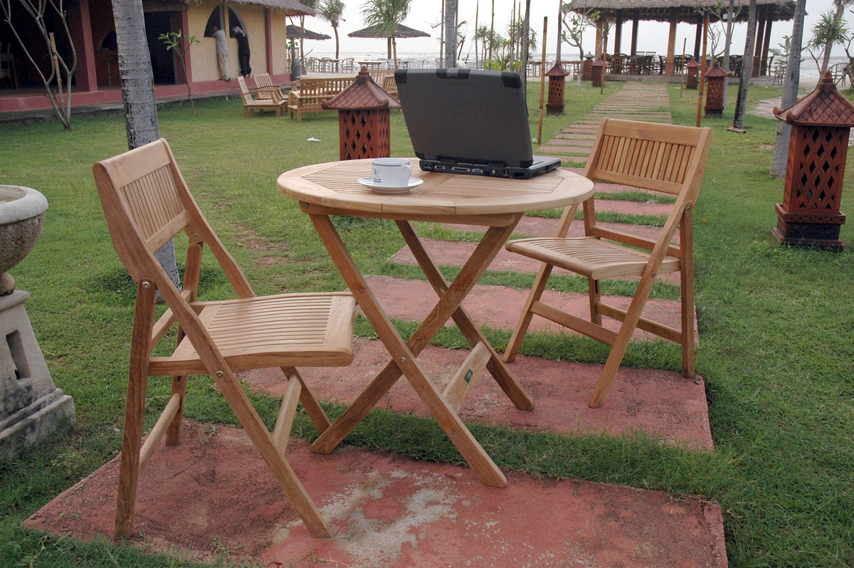 Wooden outdoor table with chairs and a laptop on a grassy area.