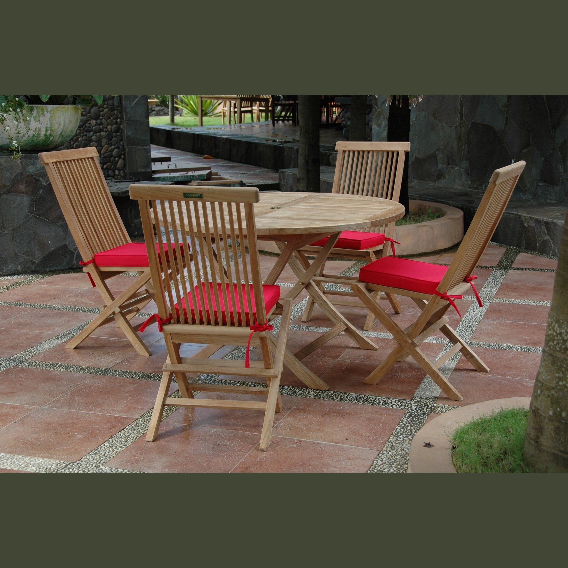 Wooden outdoor dining set with red cushions on a stone patio.