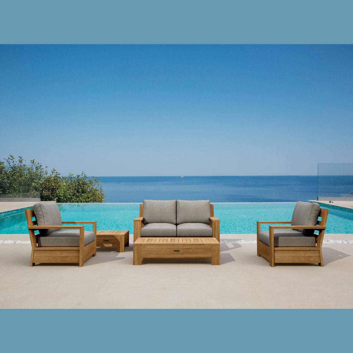 Outdoor wooden furniture set with gray cushions by a pool and blue sky.