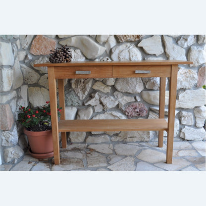 Wooden console table with two drawers against a stone wall.