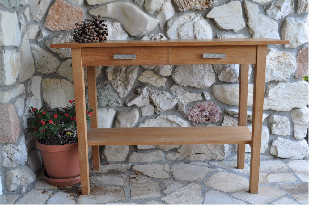 Wooden console table with two drawers against a stone wall.
