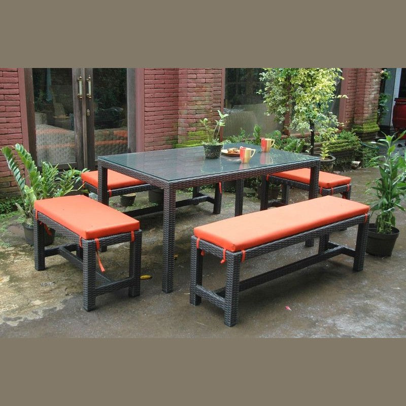 Outdoor patio set with a table and benches on a patio with plants and a brick wall in the background.