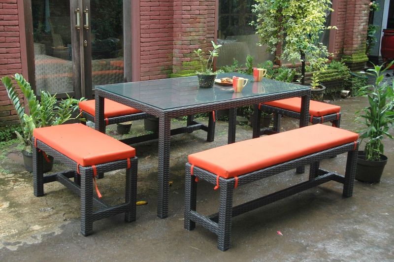 Outdoor patio set with a table and benches on a patio with plants and a brick wall in the background.