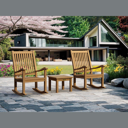Two wooden rocking chairs and a small table on a patio in front of a modern house with cherry blossoms.