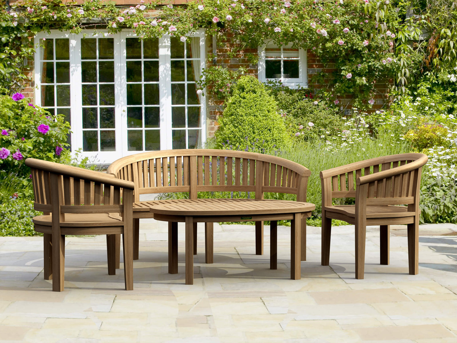 Wooden outdoor furniture set with a bench and chairs on a patio, surrounded by greenery.