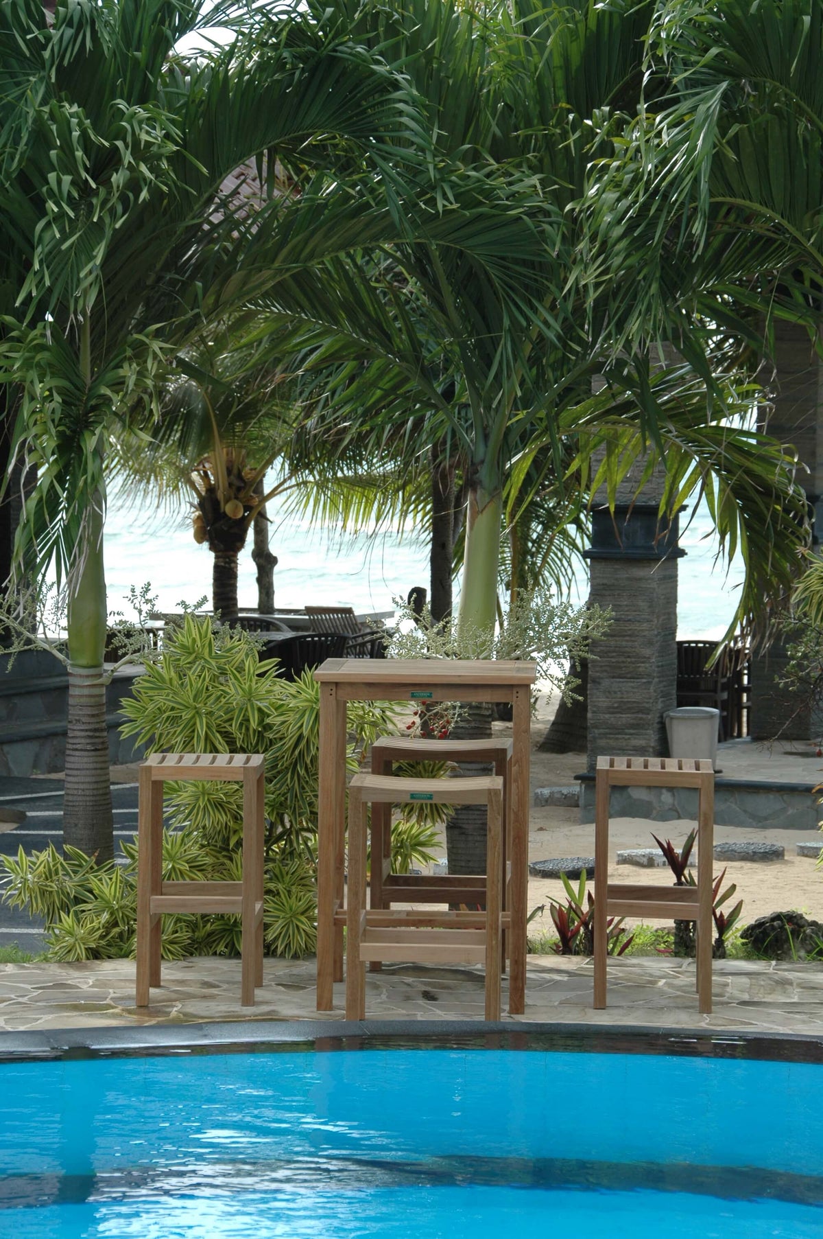 Wooden chairs and table by a poolside with palm trees in the background