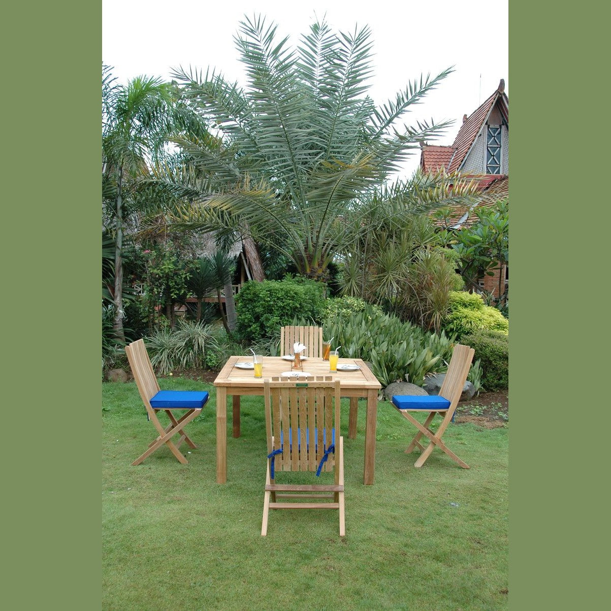 Wooden outdoor dining set with four chairs on a grassy area with palm trees in the background.