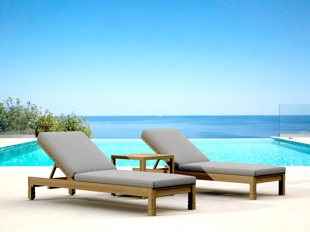 Two lounge chairs with gray cushions by a pool with a clear blue sky and ocean view.