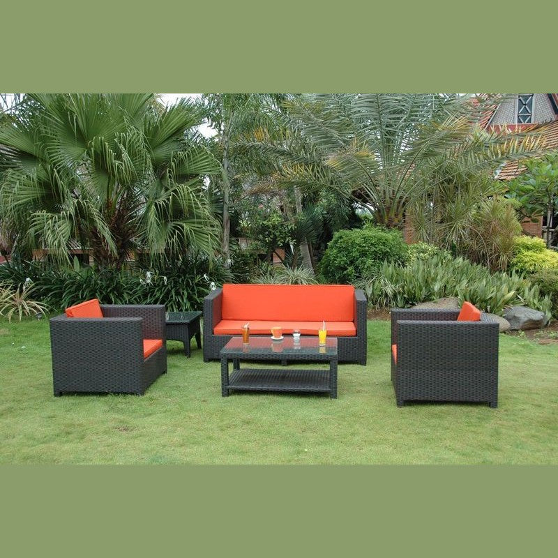 Outdoor furniture set with orange cushions on a grassy area with greenery.