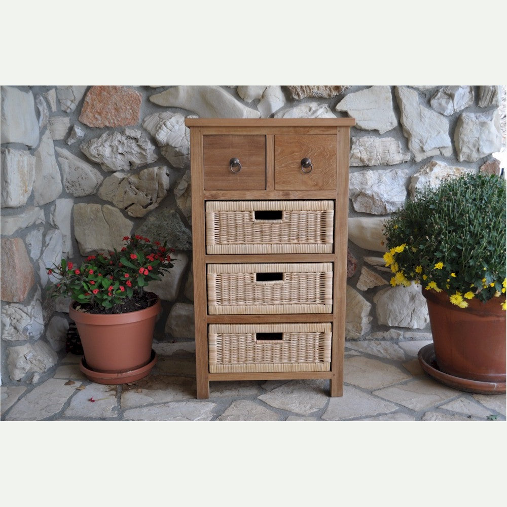 Wooden chest of drawers with wicker baskets against a stone wall with potted plants.