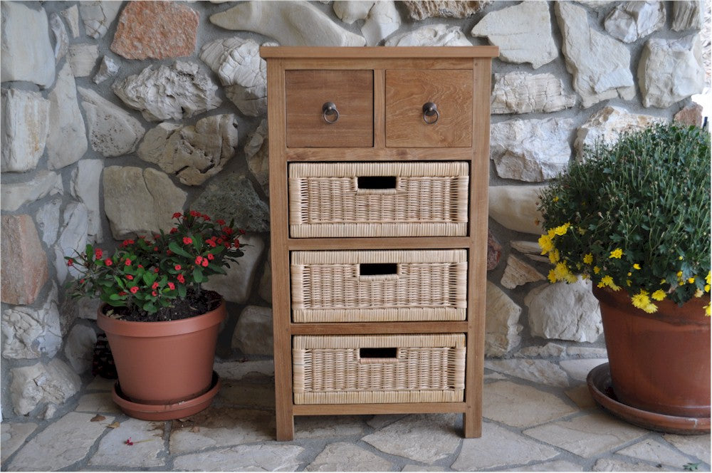 Wooden chest of drawers with wicker baskets against a stone wall with potted plants.