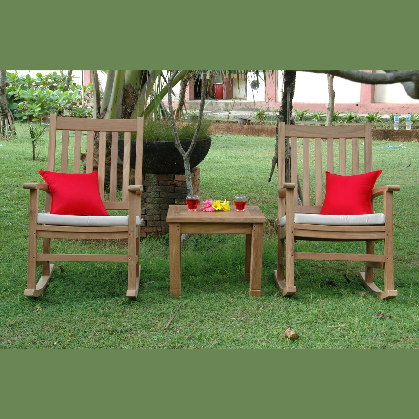 Two wooden rocking chairs with red cushions and a small table in a garden setting.
