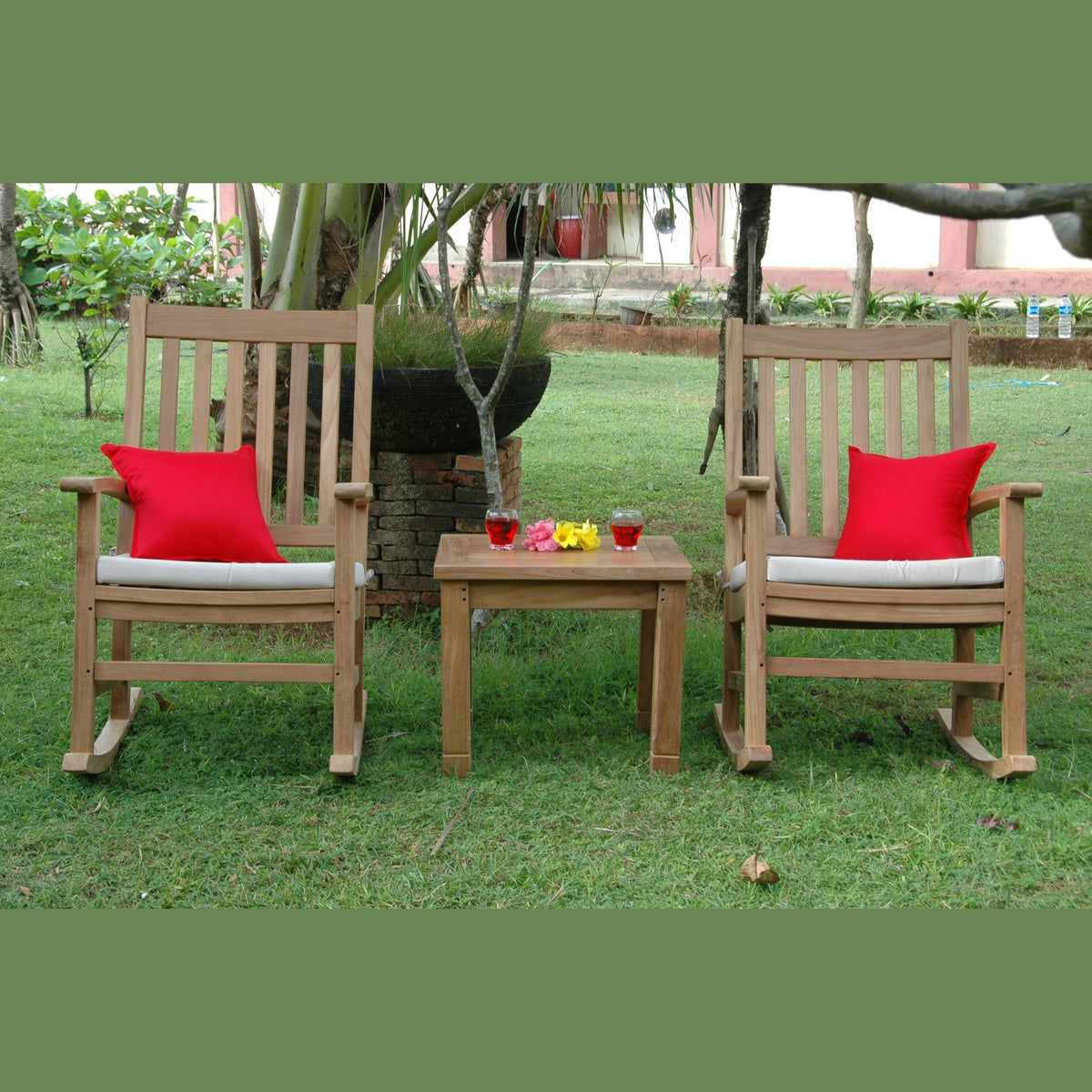 Two wooden rocking chairs with red cushions and a small table in a garden setting.