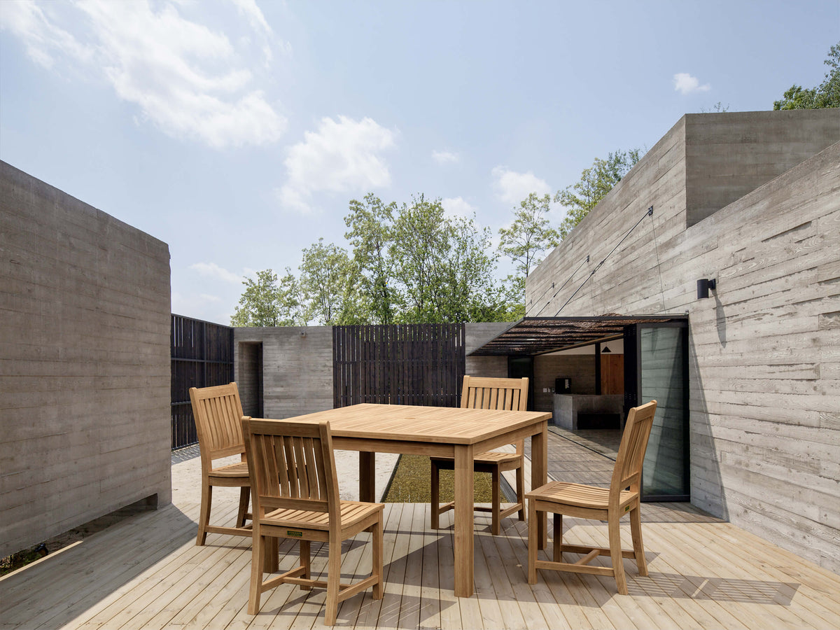 Wooden outdoor dining table with chairs in a modern architectural setting.