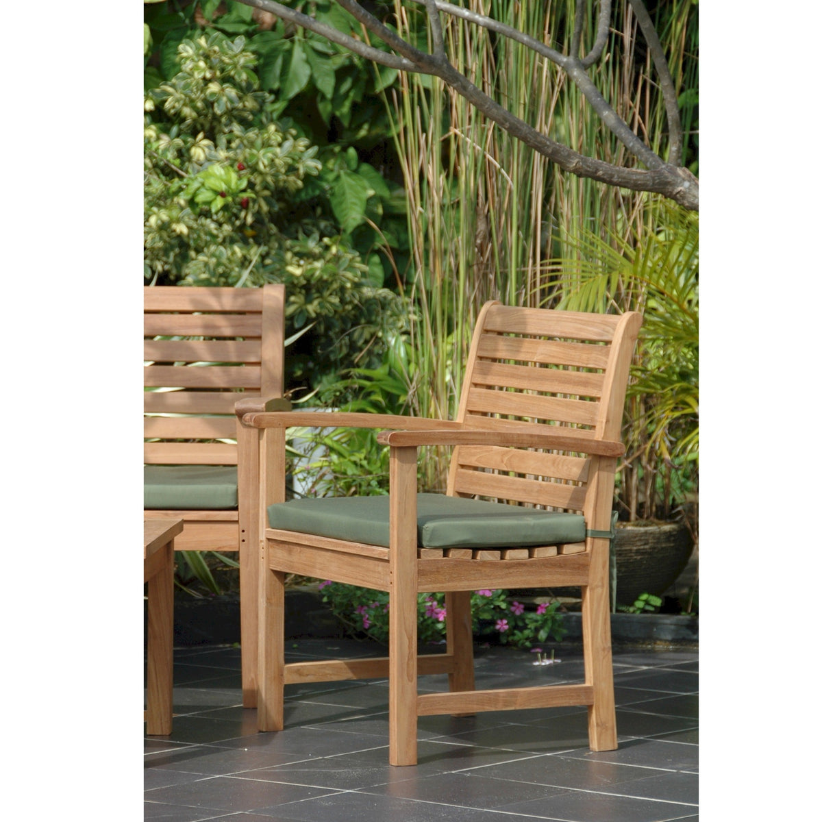 Two wooden chairs with green cushions on a patio with plants in the background