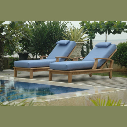 Two blue cushioned lounge chairs by a pool with greenery in the background