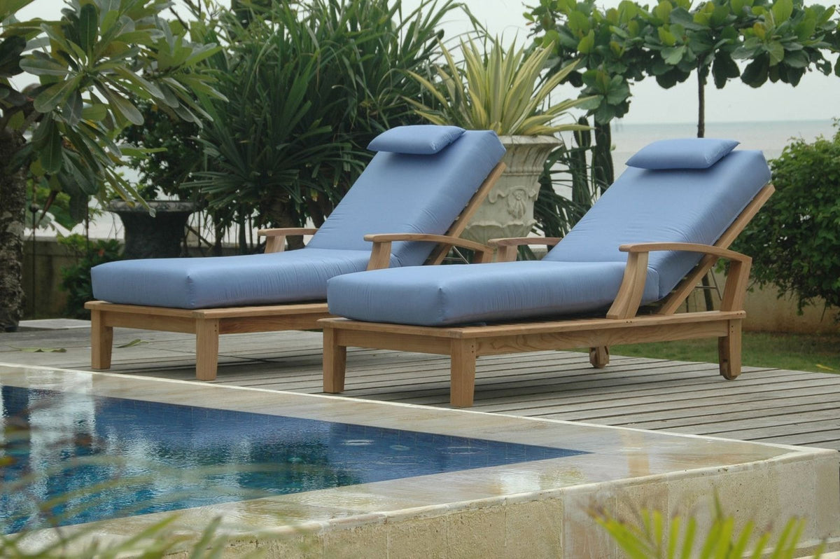 Two blue cushioned lounge chairs by a pool with greenery in the background
