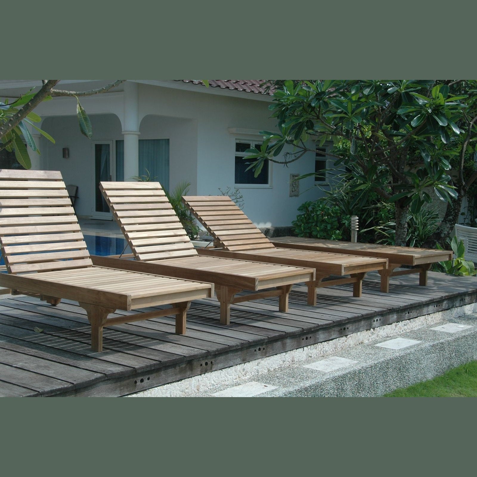 Wooden lounge chairs on a wooden deck with a building and greenery in the background