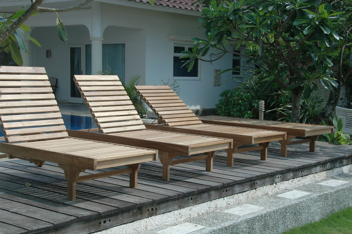 Wooden lounge chairs on a wooden deck with a building and greenery in the background