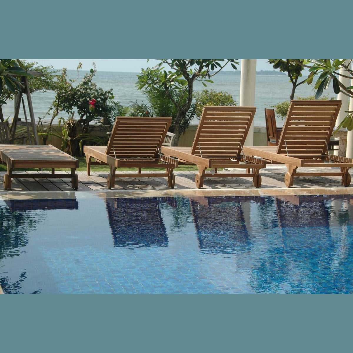 Wooden lounge chairs by a pool with a scenic view of water and trees.