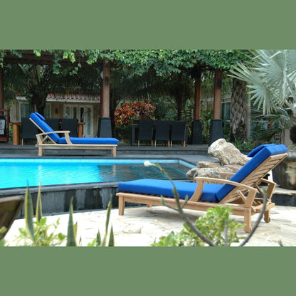 Two wooden lounge chairs with blue cushions by a poolside in a garden setting.