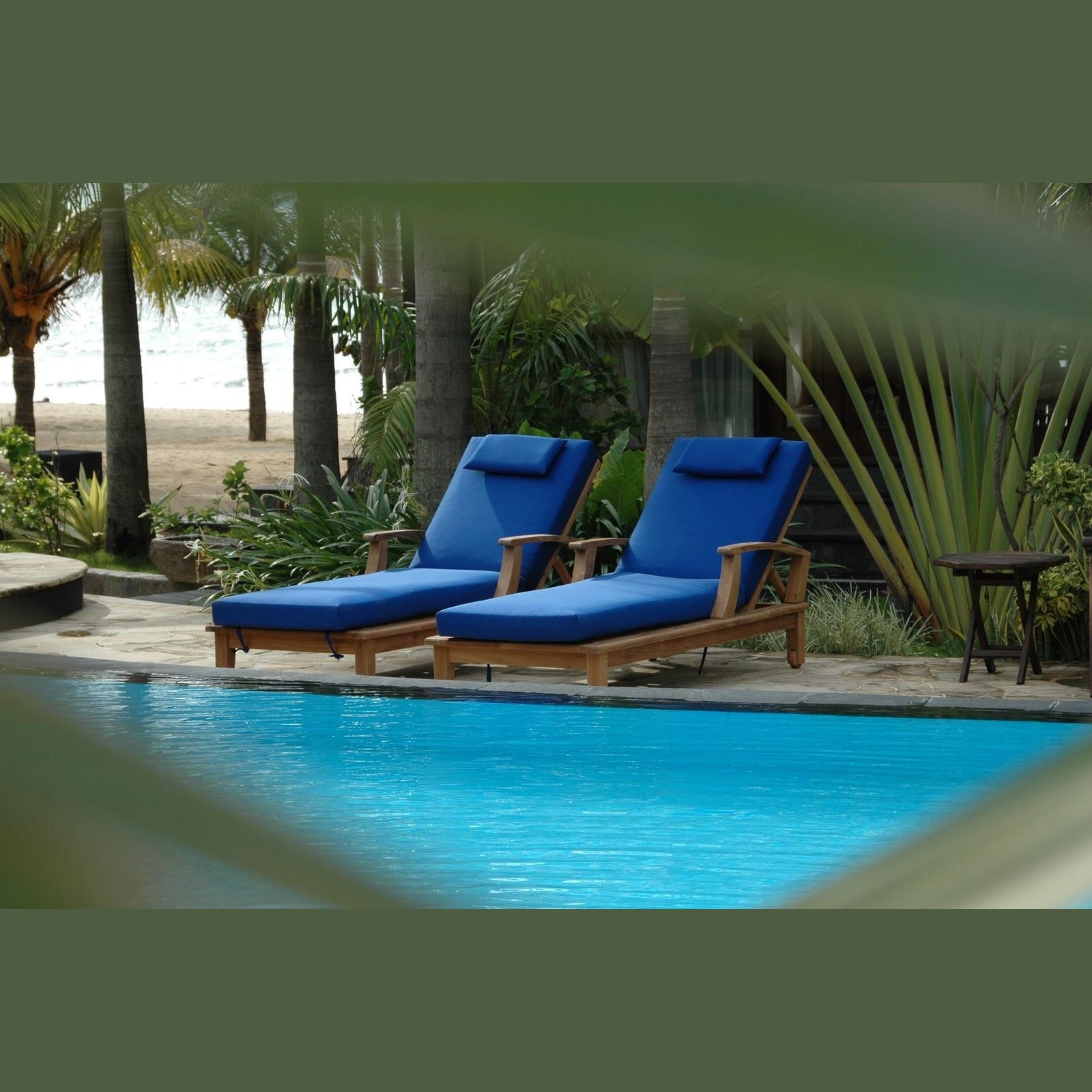Two blue lounge chairs by a pool with palm trees in the background