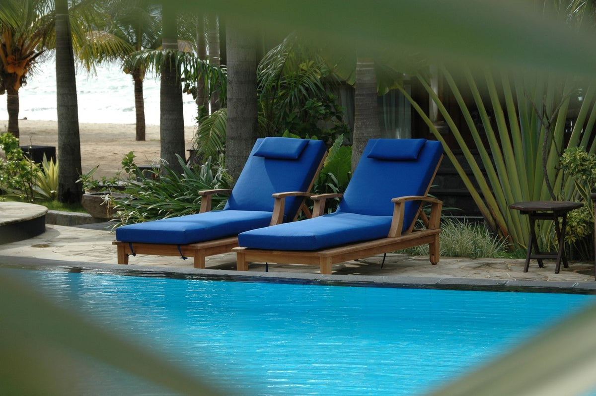 Two blue lounge chairs by a pool with palm trees in the background