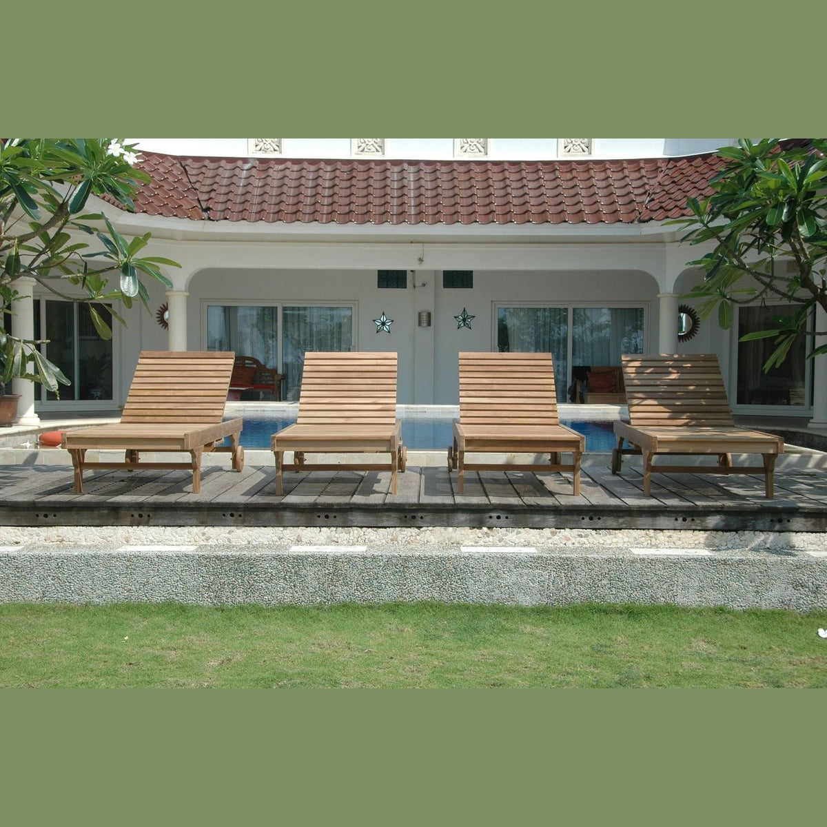 Four wooden lounge chairs by a poolside with a house in the background