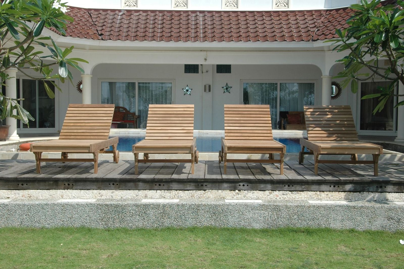 Four wooden lounge chairs by a poolside with a house in the background